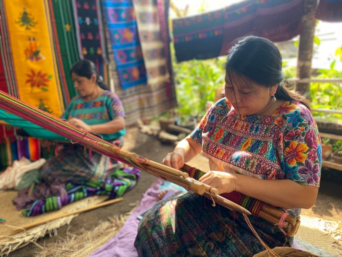 A woman wearing traditional Guatemalan clothes works a traditional weaving loom